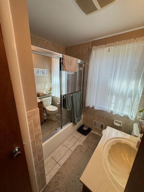 Bathroom with a toilet, shower, vanity, and window with blinds.