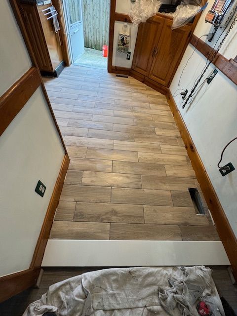 Newly installed wood-look tile flooring in a kitchen. The room includes wooden cabinets and white trim.