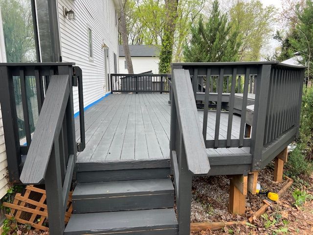 Gray painted wooden deck with black railings and steps attached to a white house.