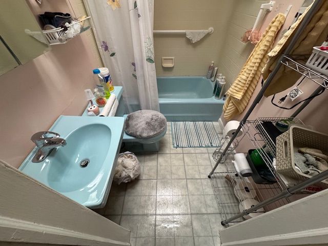 Small bathroom with turquoise sink, toilet, and bathtub. The walls are pink. A shower curtain hangs.