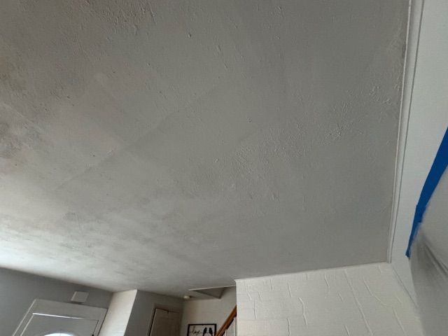Gray ceiling and white wall corner, with visible texture and a glimpse of a doorway and stairs.