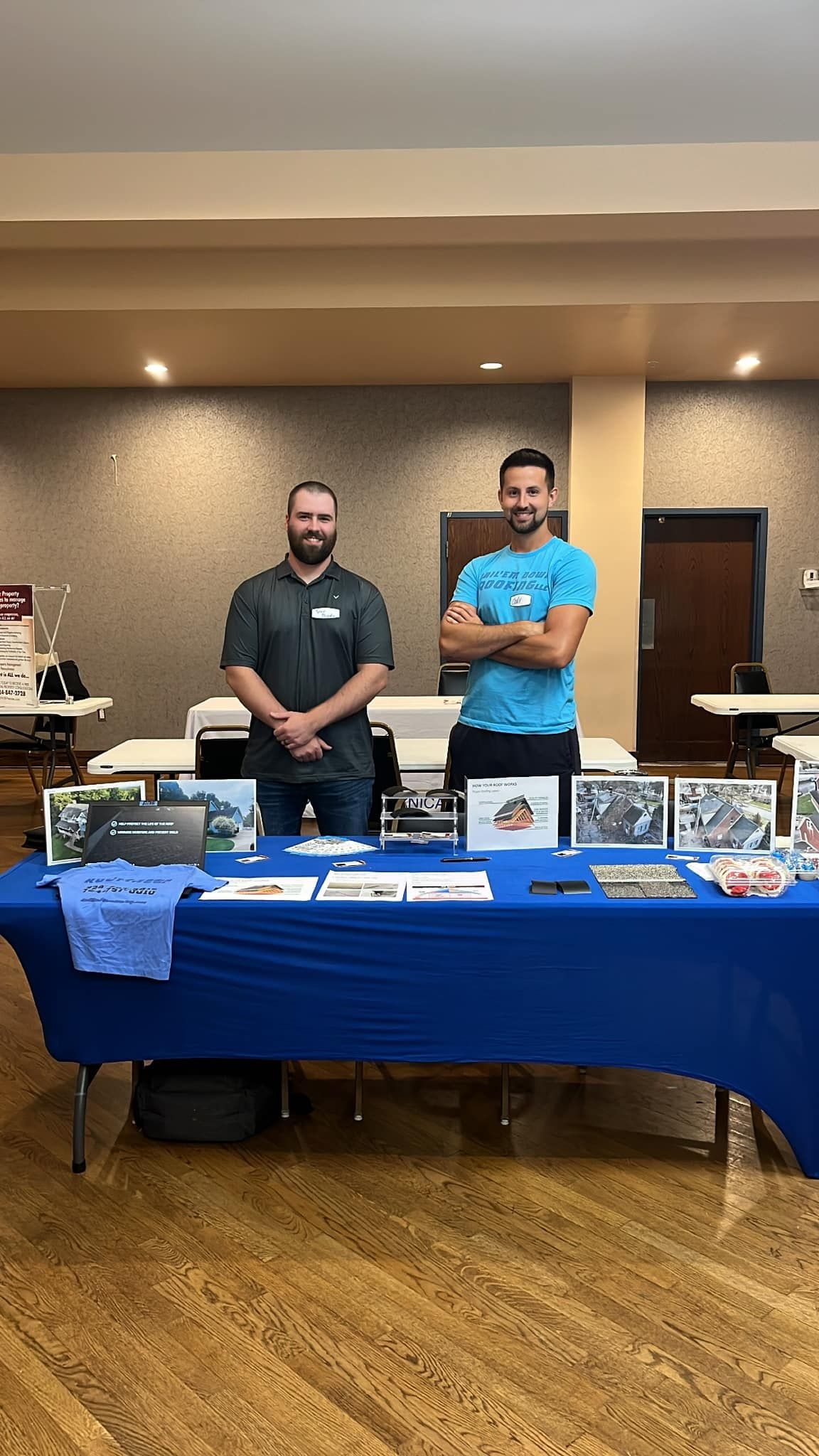 Two men are standing in front of a blue table.