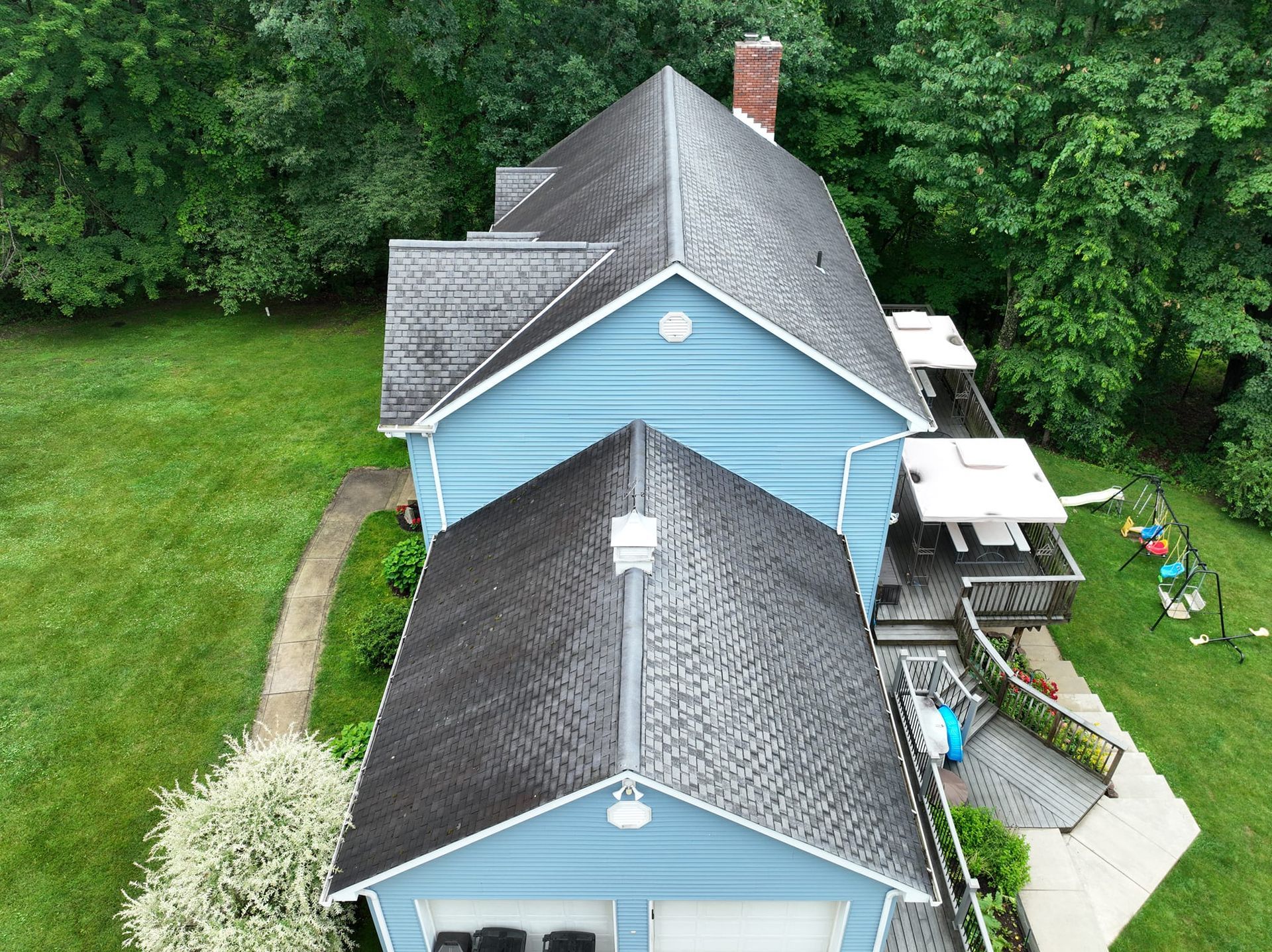 An aerial view of a blue house with a black roof surrounded by trees.