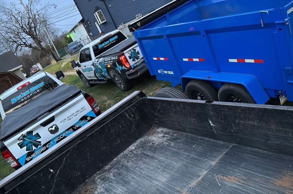 A couple of trucks parked next to each other with a blue dumpster in the back.