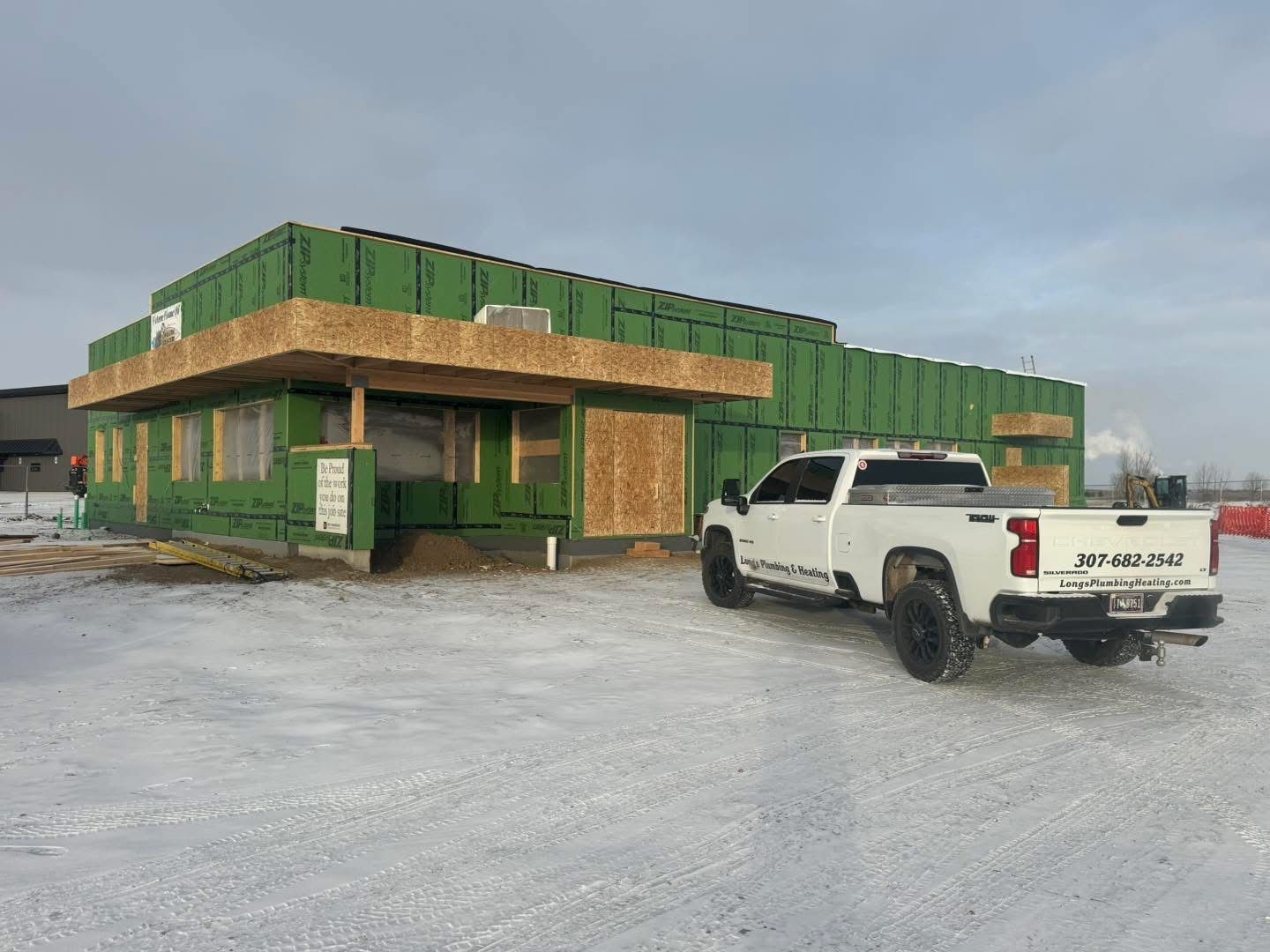 White truck parked in front of a building under construction, sheathed in green, in a snowy setting.