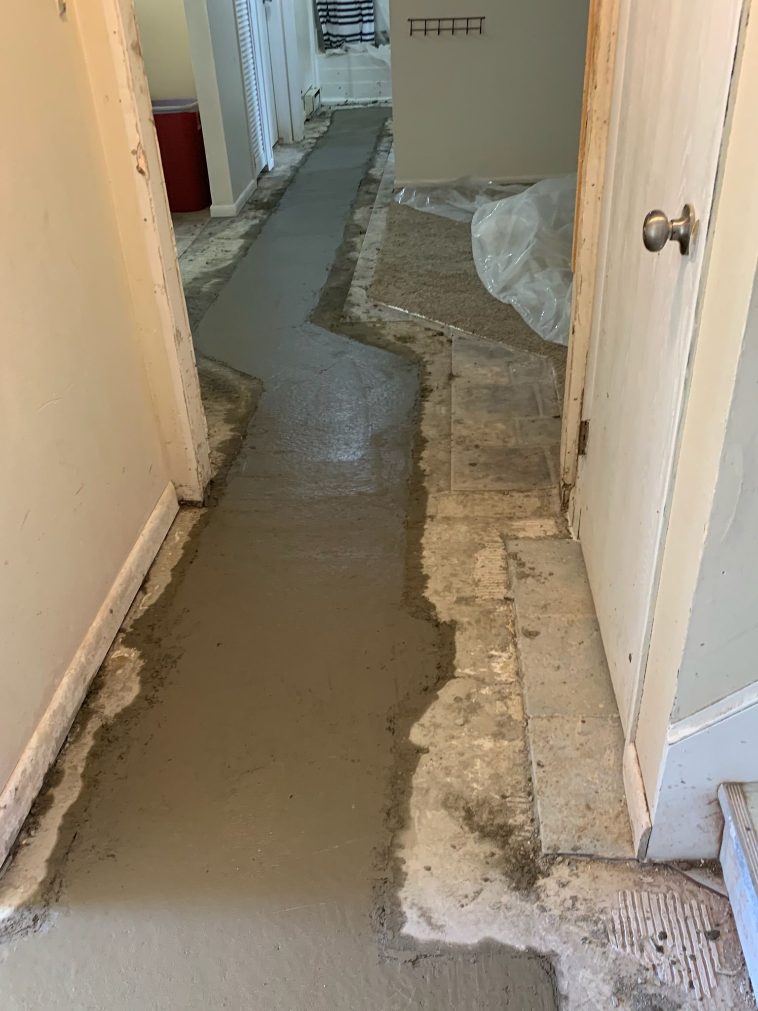 Hallway under renovation; a concrete path is laid over the floor, leading towards a doorway.