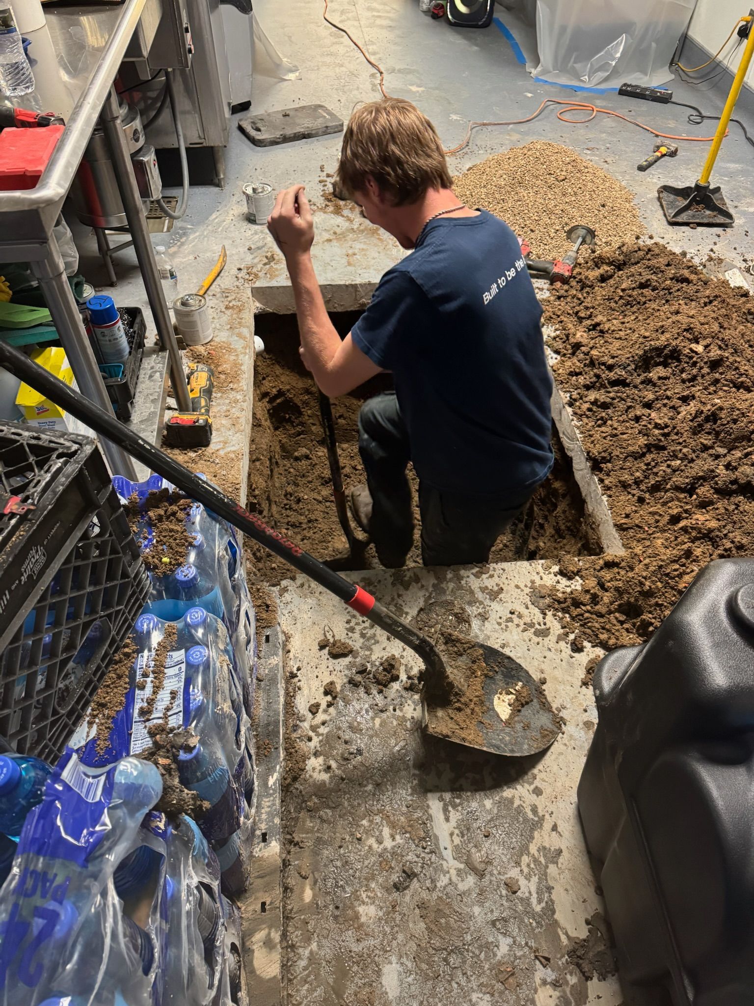 Man shoveling debris from an open floor space in a basement setting.
