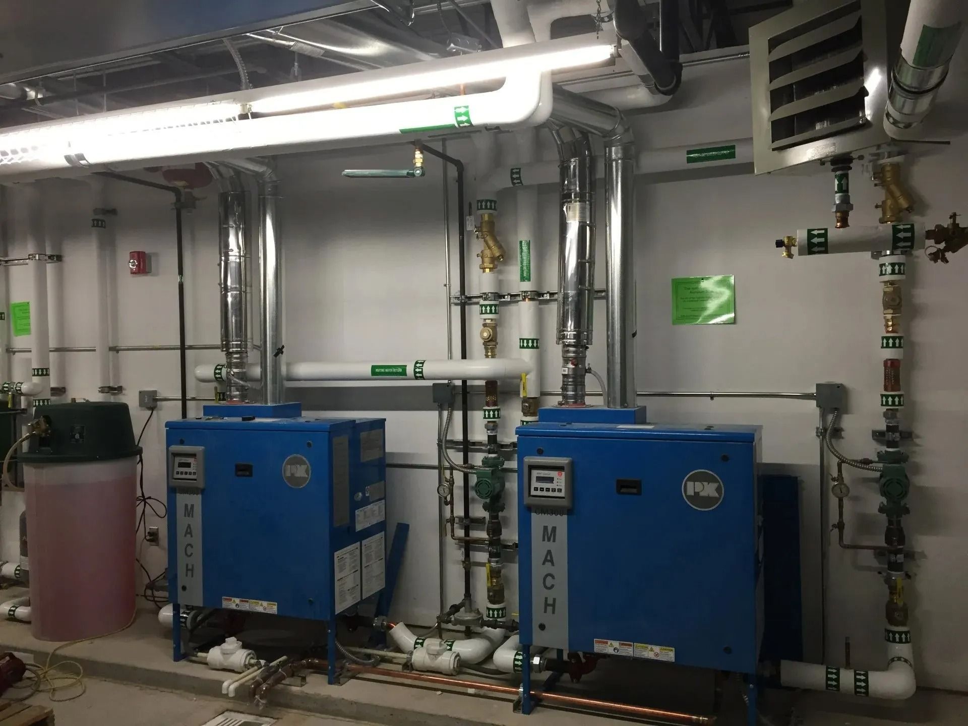 Two blue HVAC machines with pipes and a pink tank in a utility room.