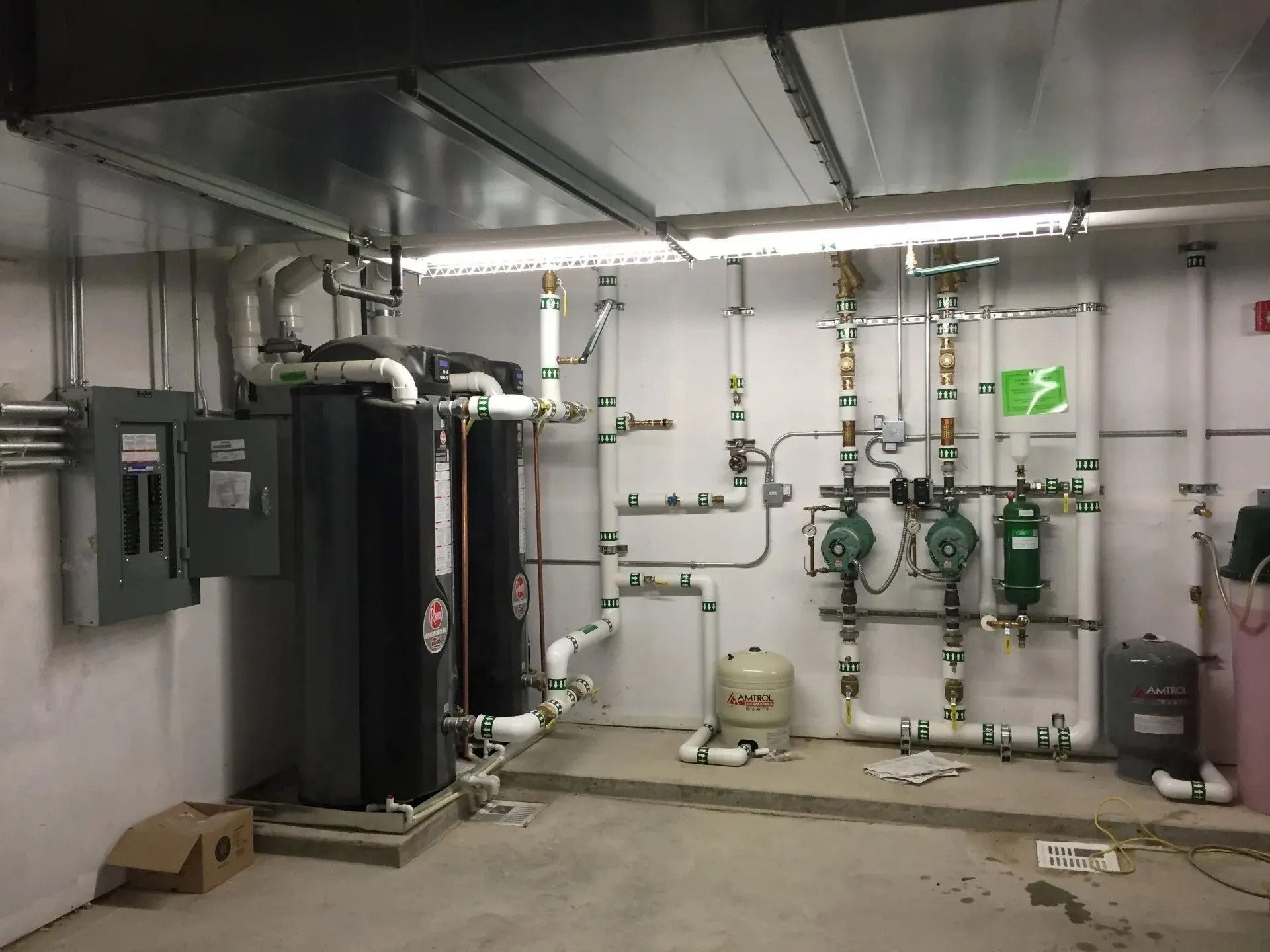 Mechanical room with black water heaters, pipes, and electrical panels.