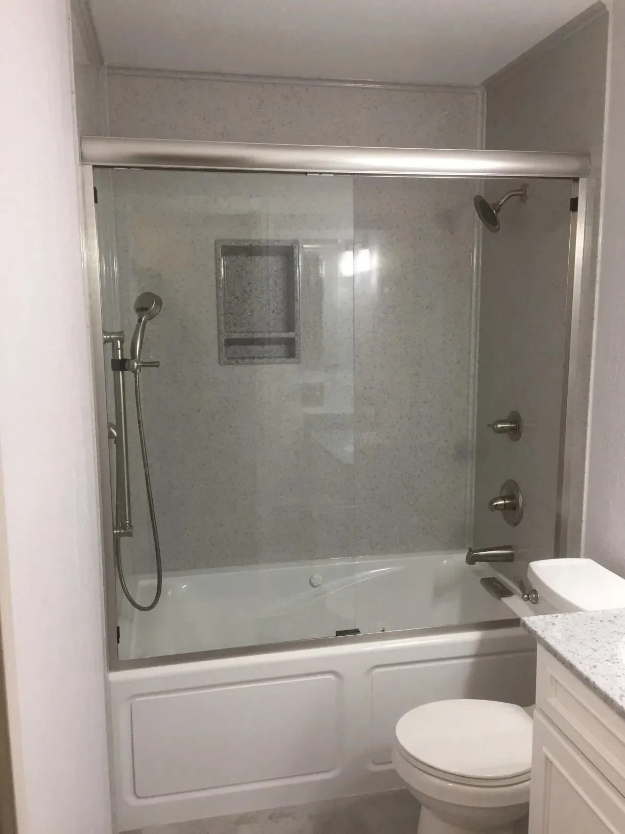 Bathroom with a white tub, shower, and toilet. Gray walls.