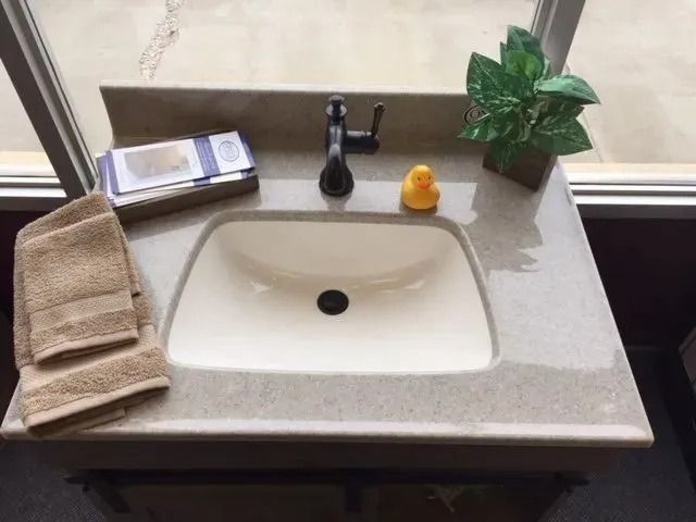 Bathroom vanity with beige countertop, white sink, faucet, towels, rubber duck, and a small plant.