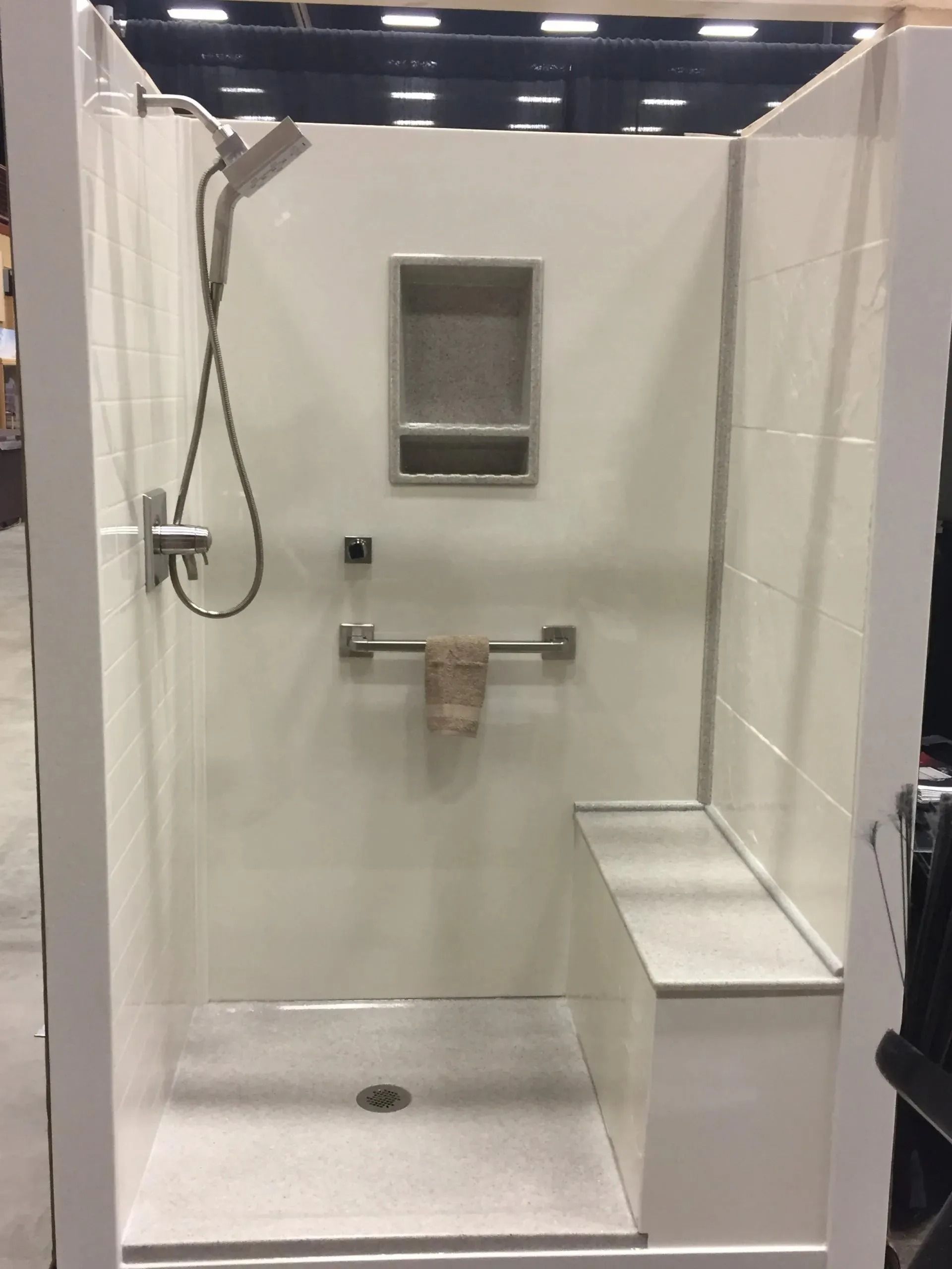 White accessible shower with hand-held showerhead, built-in seat, and grab bar.