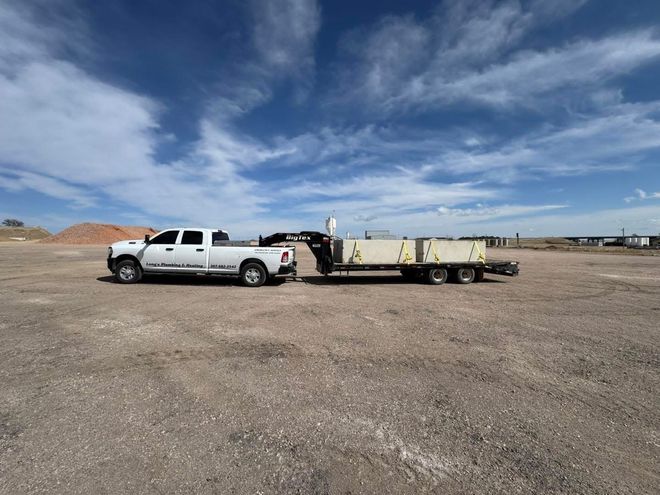 White truck towing a trailer on a dirt field under a blue sky with clouds.