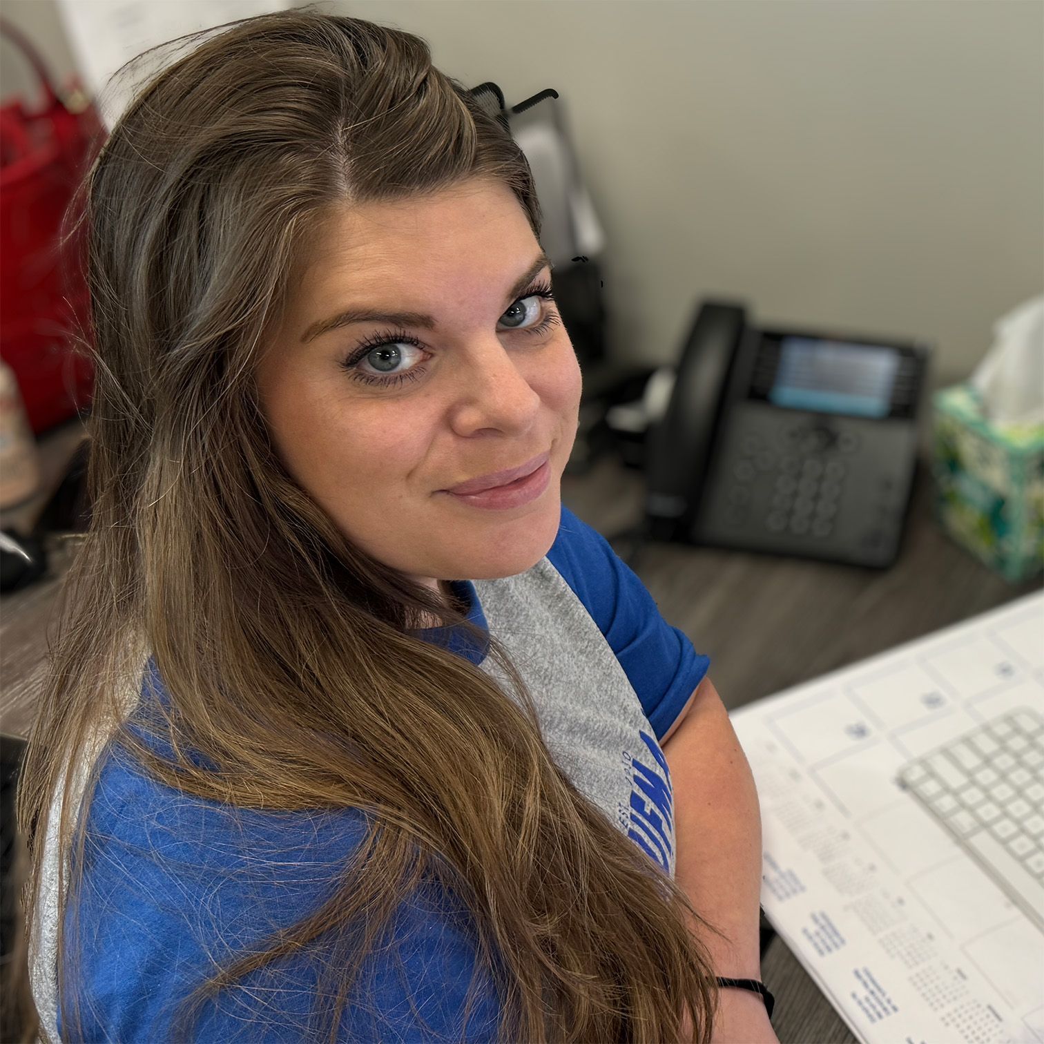 A woman in a blue shirt is smiling in front of a computer