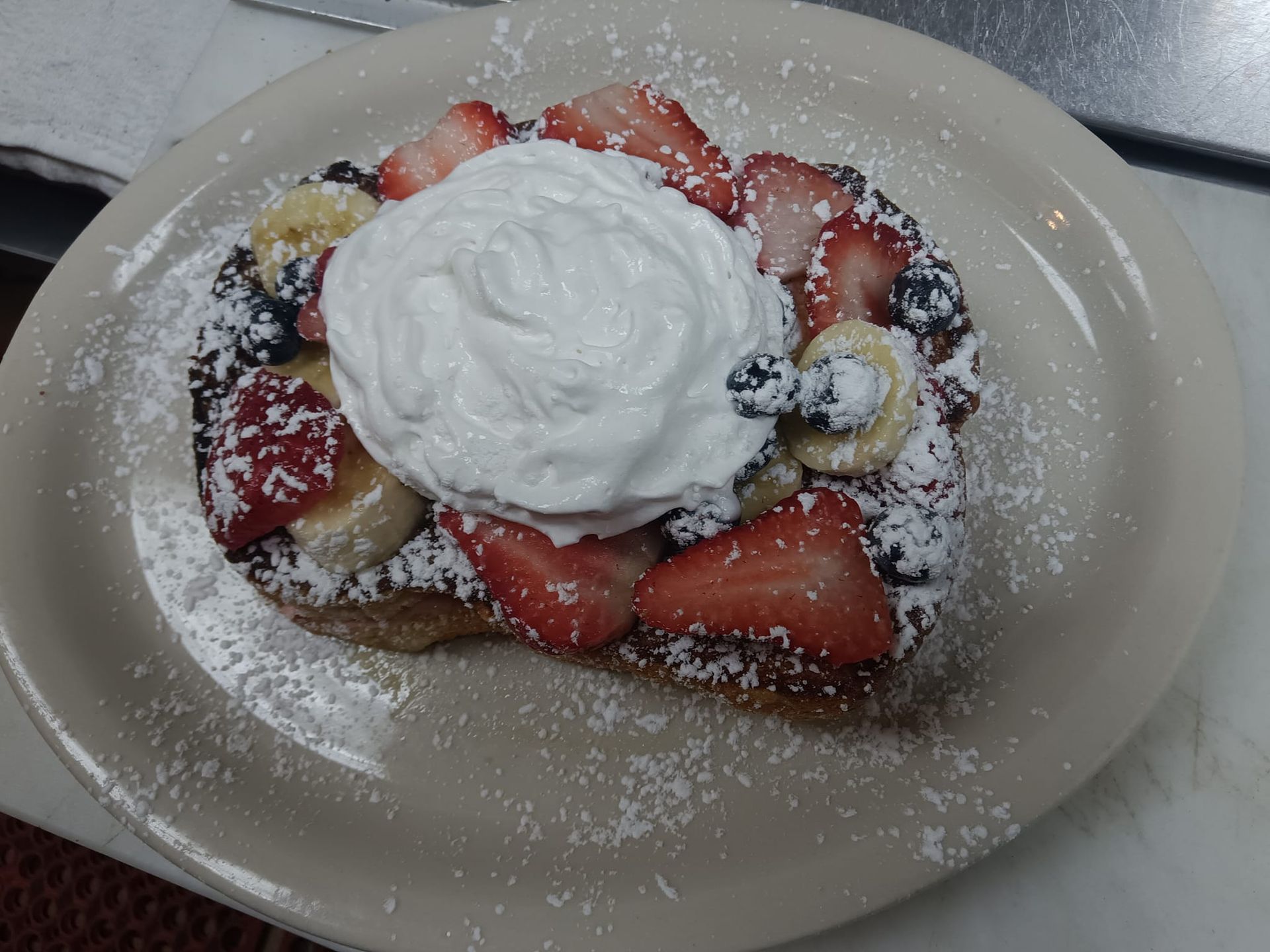 French toast with strawberries bananas blueberries and whipped cream on a plate