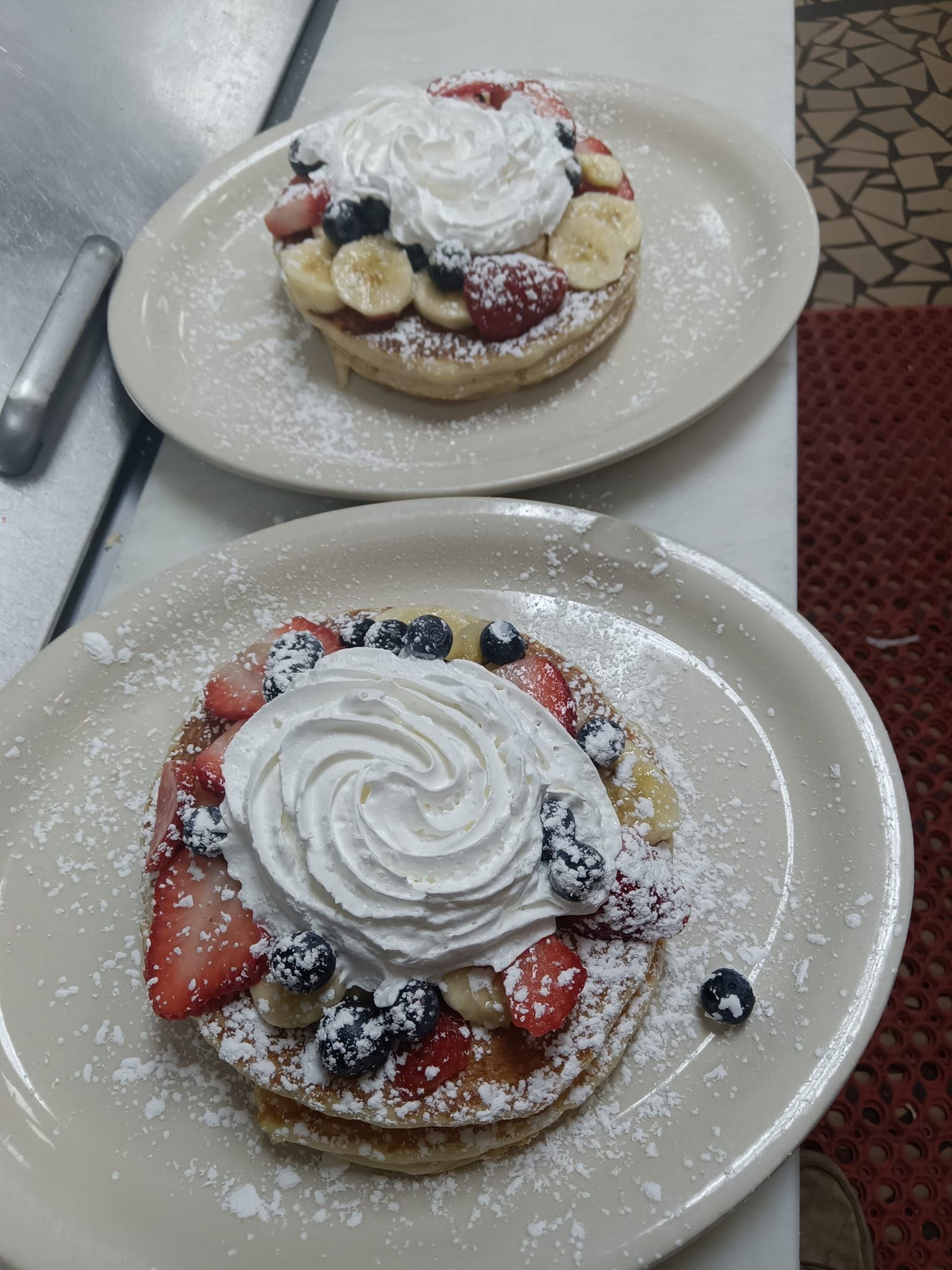Two plates of pancakes with whipped cream and fruit on them.