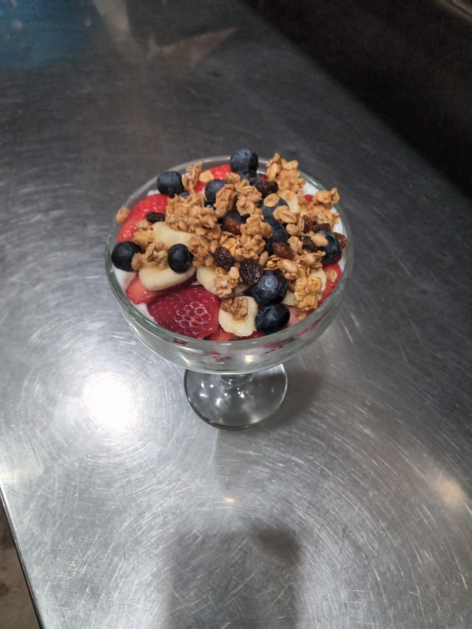 A glass bowl filled with strawberries , blueberries , bananas and granola.