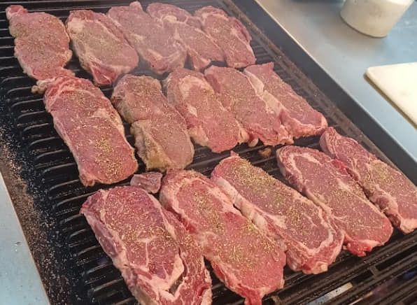 A bunch of steaks are cooking on a grill