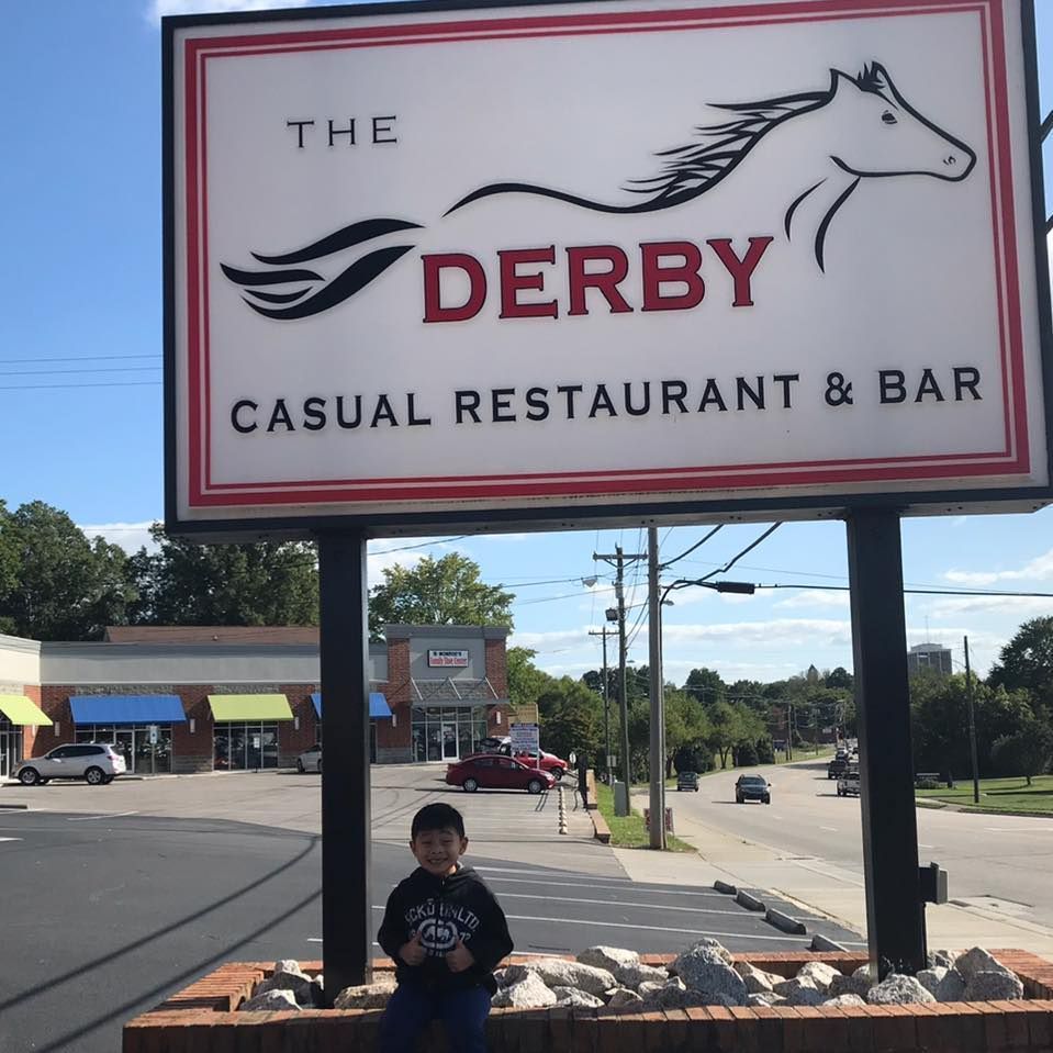 A little boy sits under a sign for the derby casual restaurant and bar