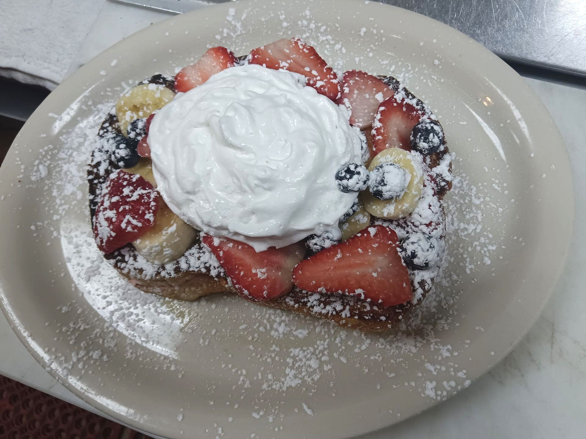 French toast with strawberries bananas blueberries and whipped cream on a plate