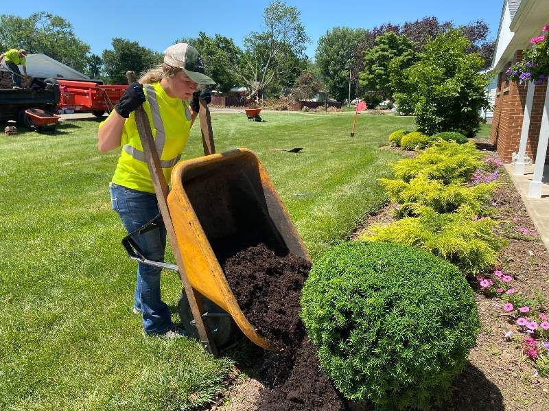 A woman is pushing a wheelbarrow full of dirt in a garden.