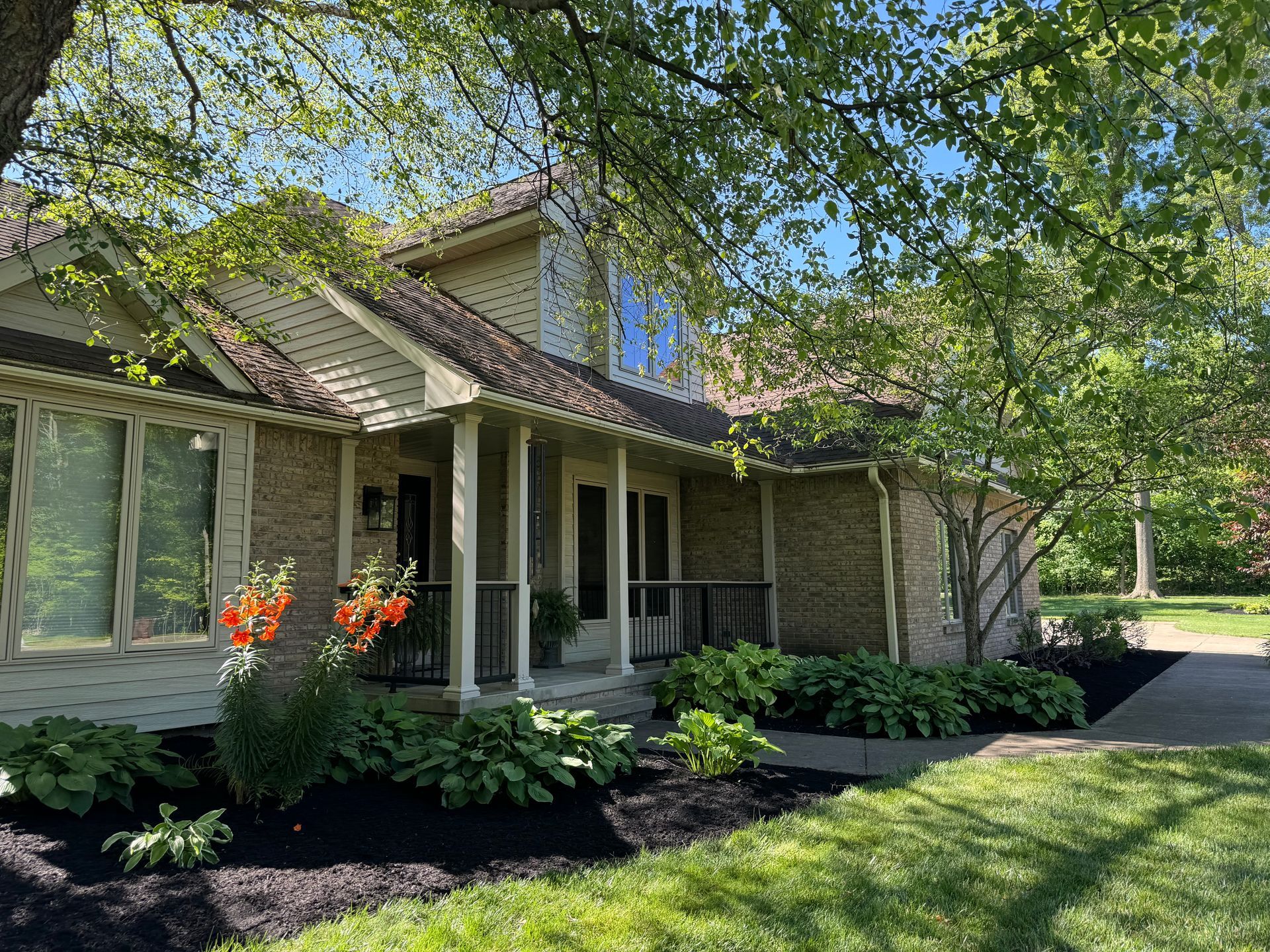 A large brick house with a porch and trees in front of it.