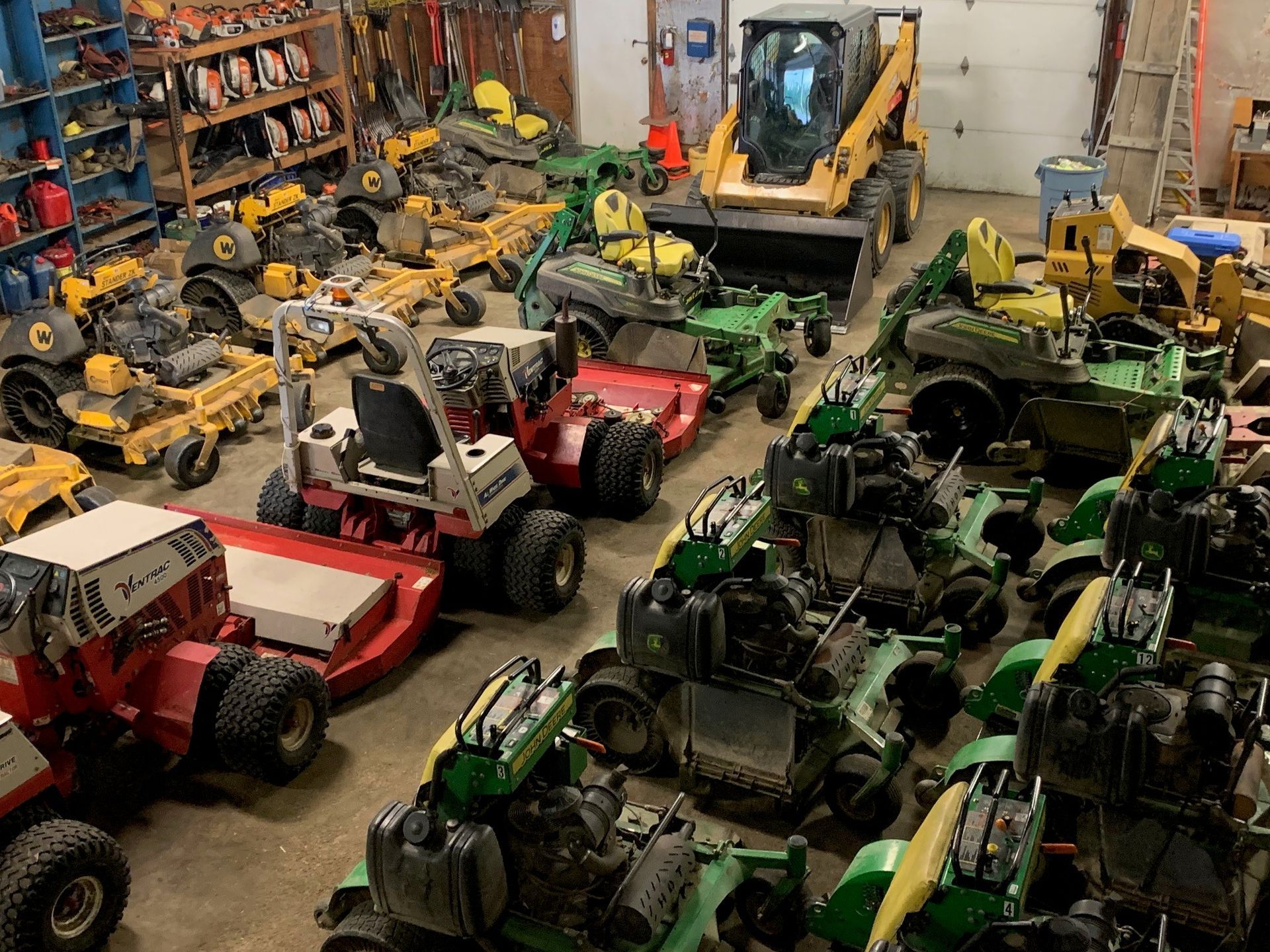 A bunch of lawn mowers are parked in a garage.