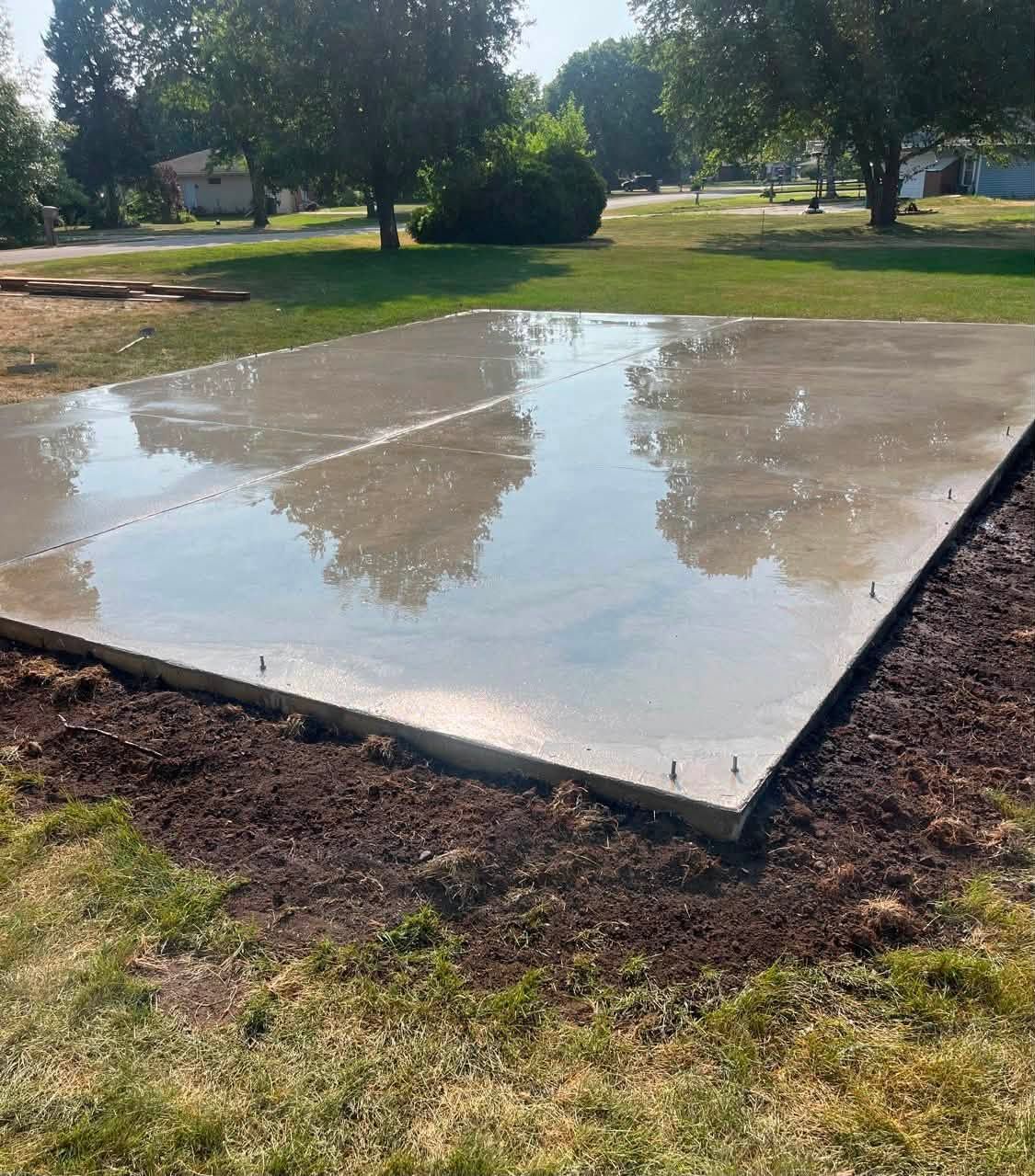 Wet concrete slab in a park, reflecting trees and sky on a sunny day