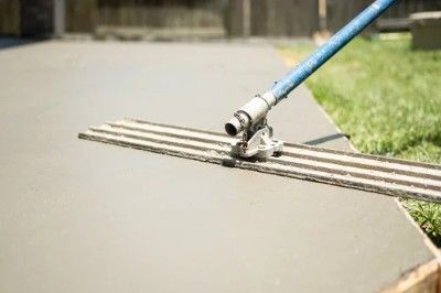A man leveling a wet concrete surface beside green grass.
