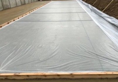 Large concrete slab covered with plastic sheeting and wooden formwork at the edges