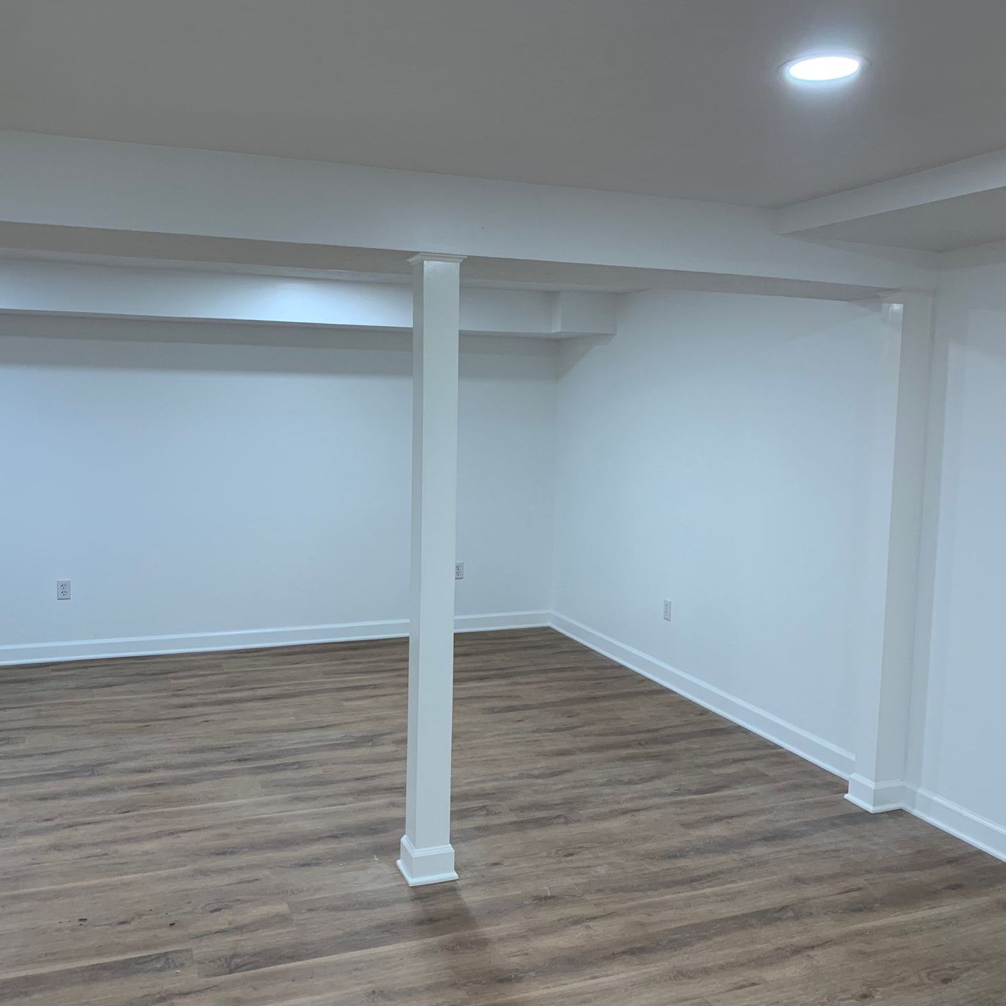 An empty basement with hardwood floors and white walls.