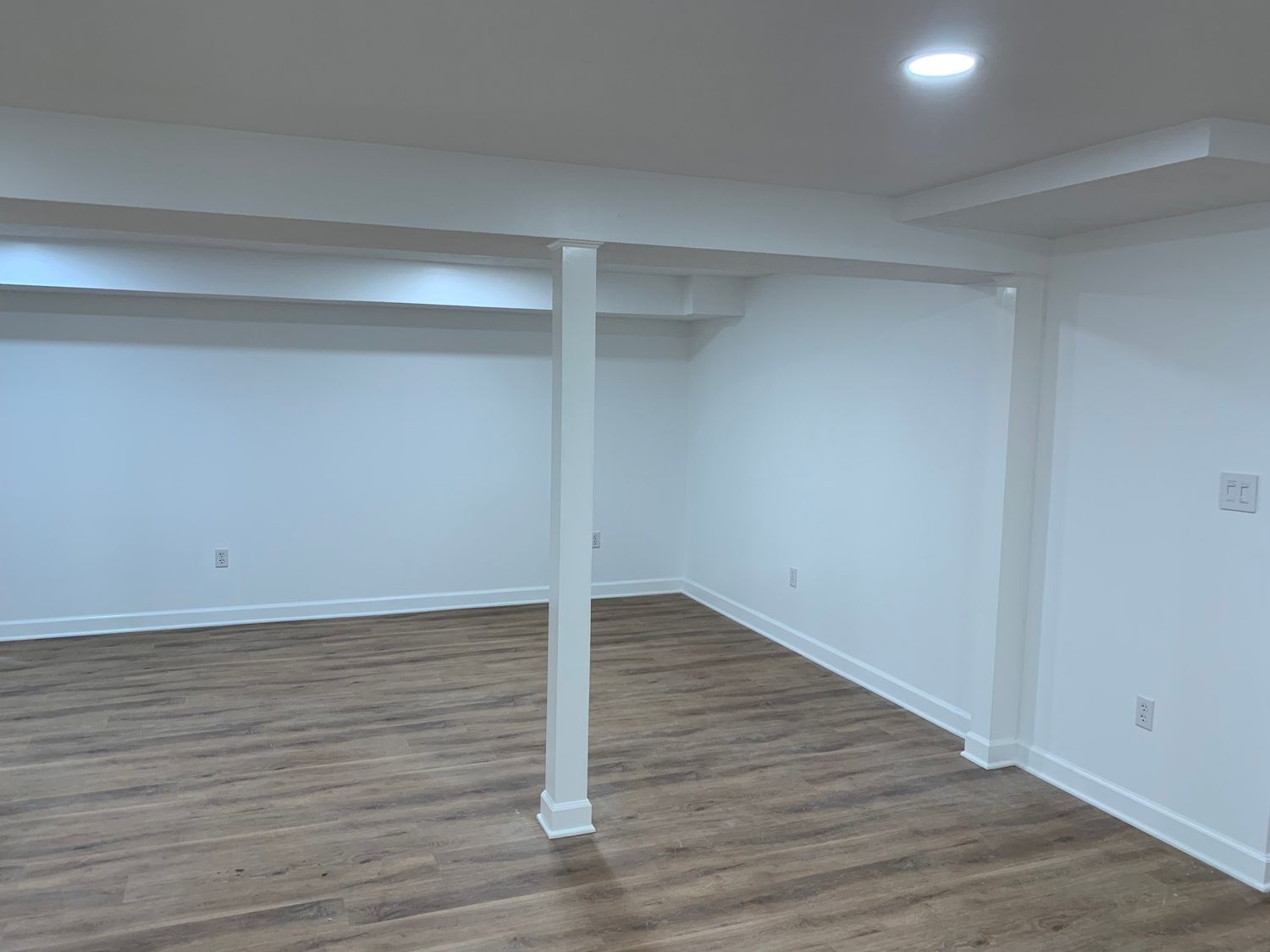 An empty basement with hardwood floors and white walls.