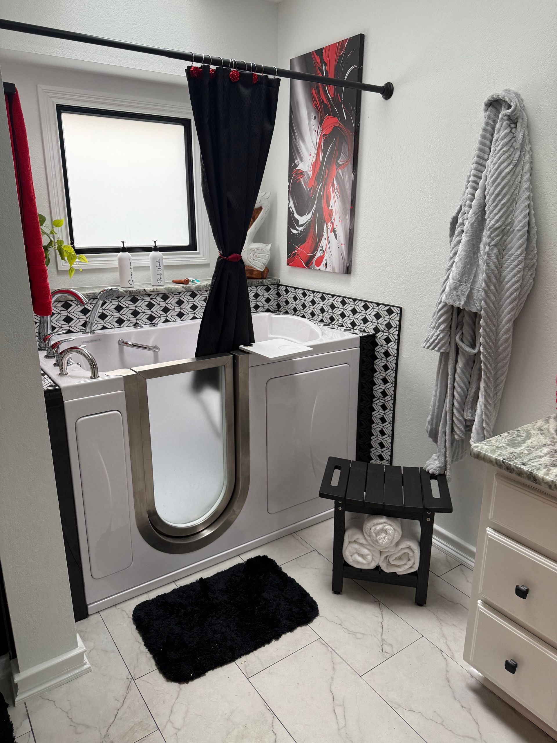 Accessible bathroom with walk-in tub, black accents, black rug, gray robe, and a small black stool.