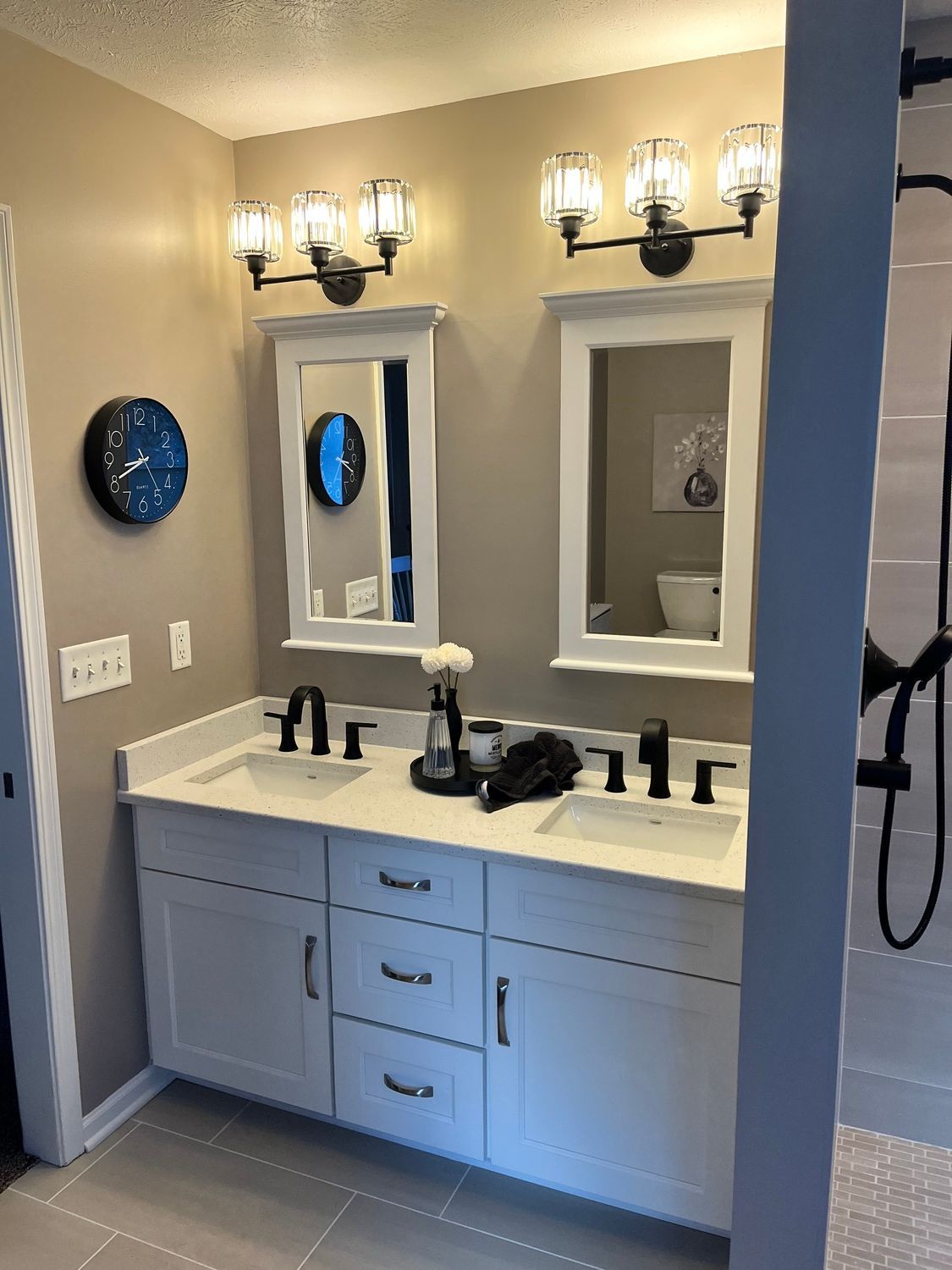 A bathroom with two sinks , two mirrors , a clock and a shower.