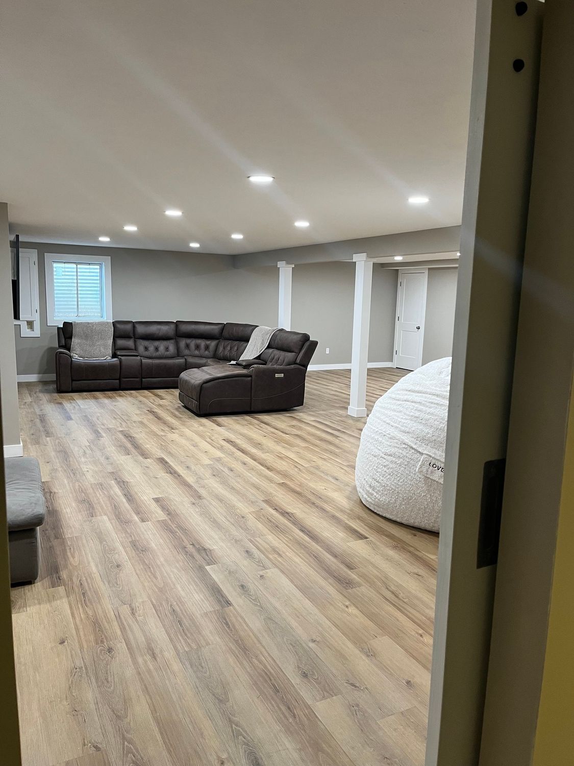 A living room in a basement with hardwood floors and a sectional couch.