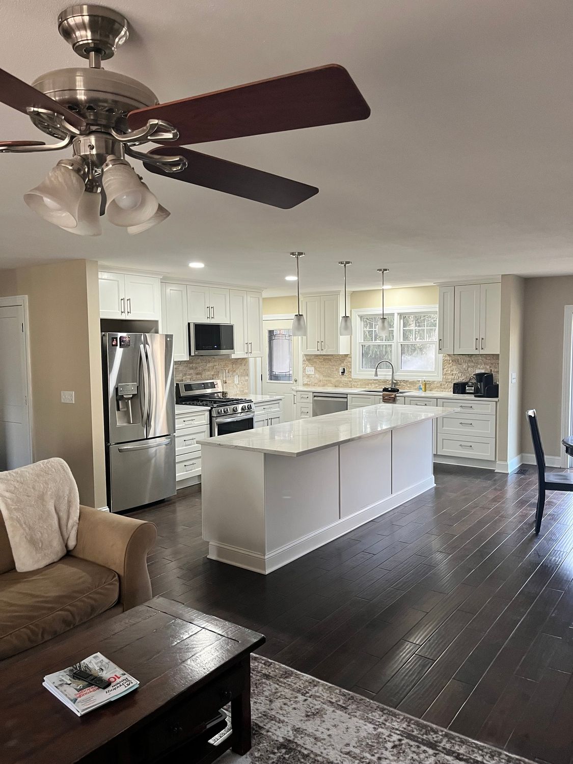 A living room filled with furniture and a kitchen with a ceiling fan.