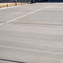 Empty concrete roadway with white lane markings beside a chain-link fence.