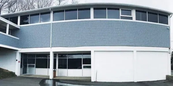 Curved modern building facade with blue siding, large windows, and white lower walls