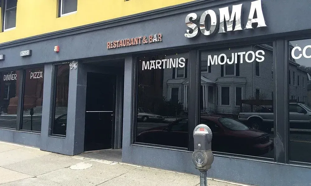 Storefront of SOMA restaurant/bar with black windows and signs for Martinis and Mojitos on a city sidewalk