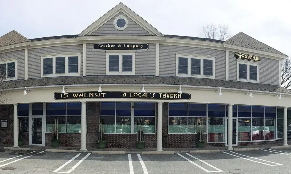 Two-story gray storefront with black awnings and a parking lot in front