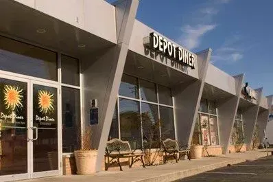 Storefront with angular gray facade, glass windows, and sun-logo signs outside Depot One furniture store.