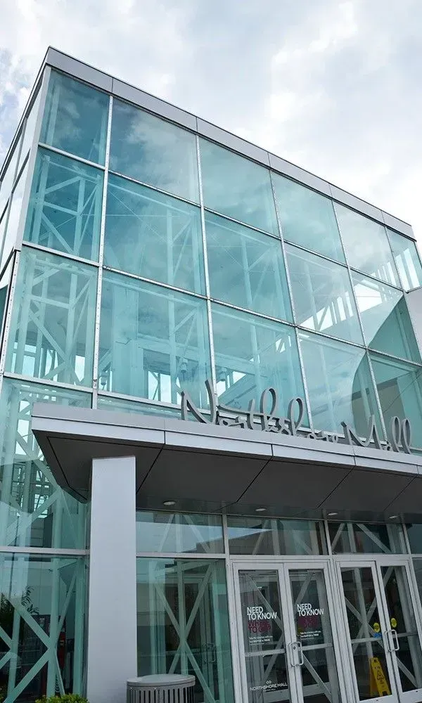 Glass-fronted modern building entrance with white pillars and metal framework under a cloudy sky