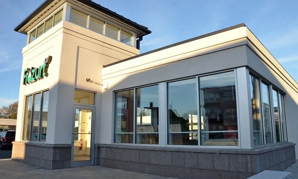 Modern storefront with large glass windows and a white tower entrance at dusk
