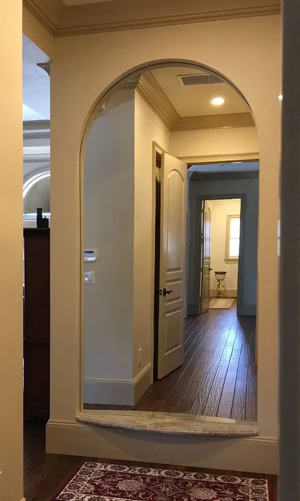 Hallway with arched doorway, beige walls, and wood floor leading to a lit interior room