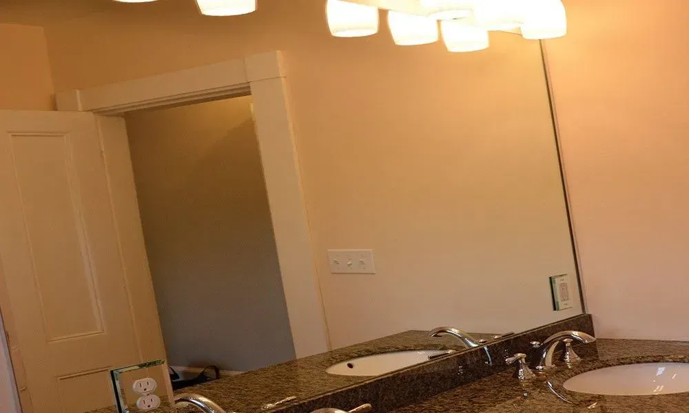 Bathroom vanity with granite countertop, sink, mirror, and overhead lights against beige walls.