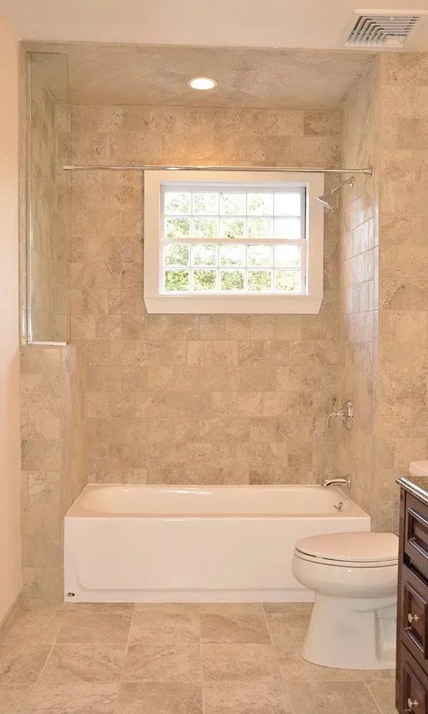 Beige tiled bathroom with a bathtub, toilet, and small window.