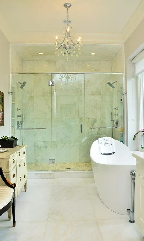 Elegant white bathroom with glass shower, freestanding tub, chandelier, and large windows