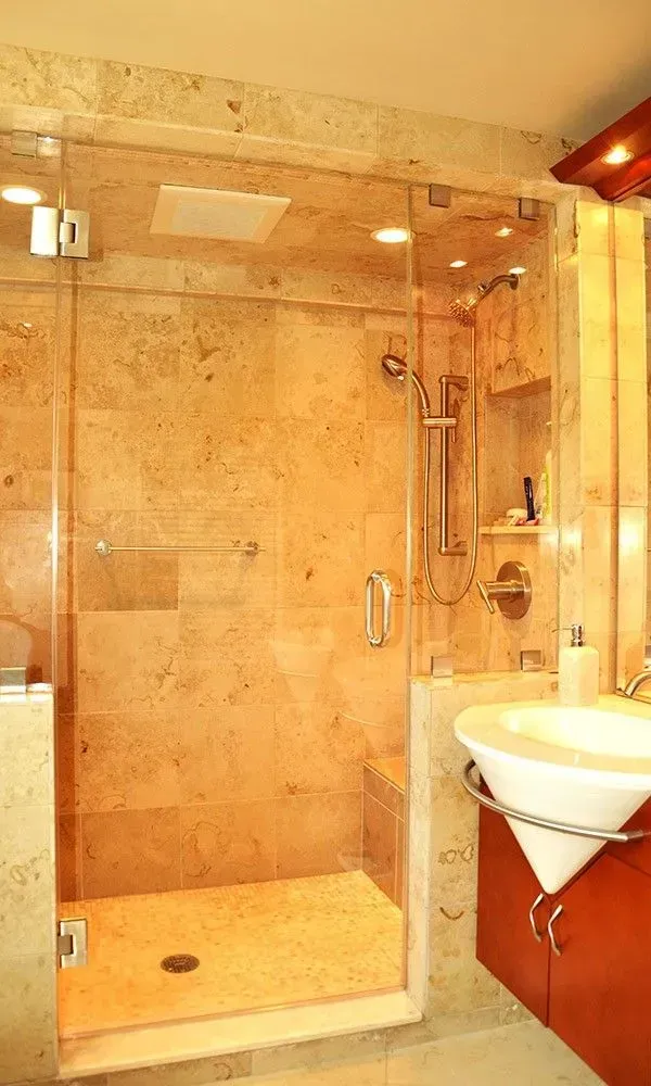 Glass shower stall and white sink in a beige-tiled bathroom with warm lighting