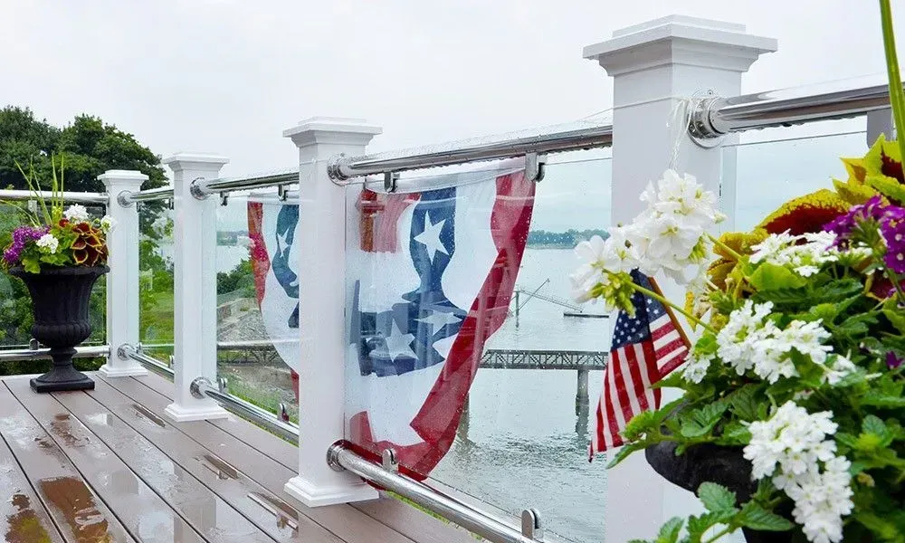 Patriotic bunting and U.S. flags on a white deck railing with flowers and water beyond