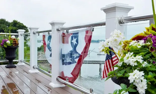 Patriotic bunting and American flags on a white deck railing beside white flowers and a water view
